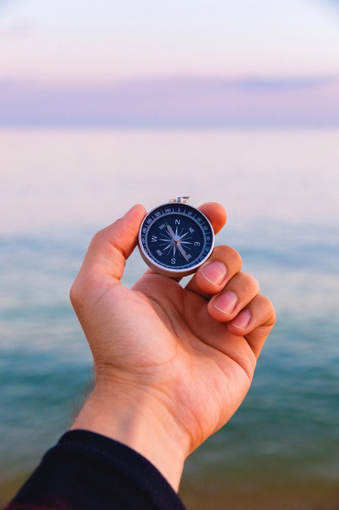 Hand holding compass with ocean and purple sky in backdrop - Executive Leadership Coach Business Career in Pennsylvania Donna Spina Coaching InDeed